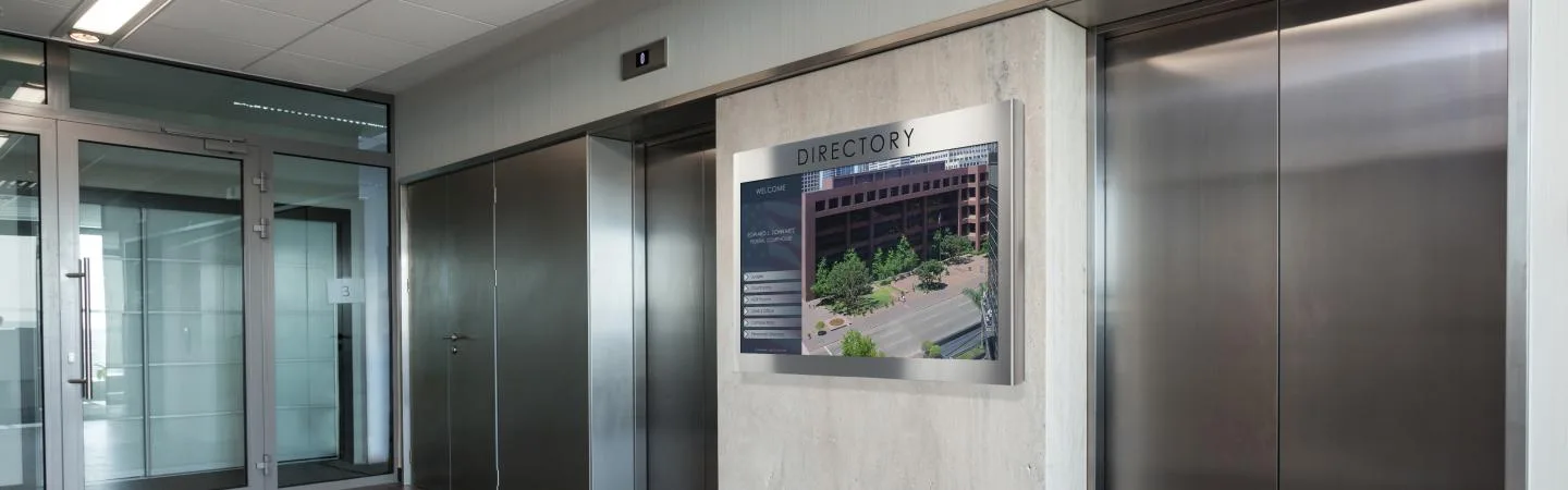 Office building elevator bank with commercial digital signage screen that reads "Directory," showing office photo.