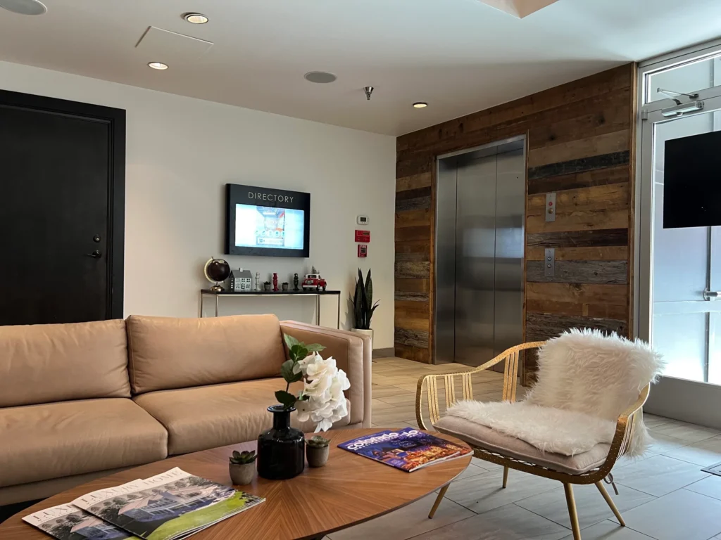 A small commercial office building lobby with a tan chair and couches, and a digital building directory on the wall.