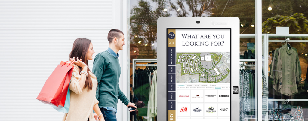 Shopper couple walks nearby silver outdoor digital information kiosk seen as way to revolutionize retail spaces.