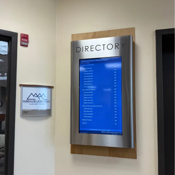 Directory sign with a blue listing screen mounted on a wall in a medical building lobby.