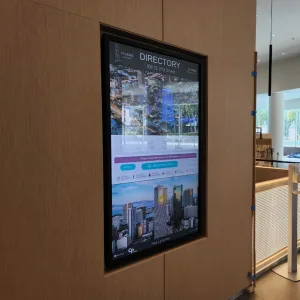 touchsource-keystone-65-inch-digital-directory - TouchSource - TouchSource Digital lobby directory screen embedded in wood paneling, showing the word 'DIRECTORY' and the address 100 SE 2nd Street (interactive touchscreen).