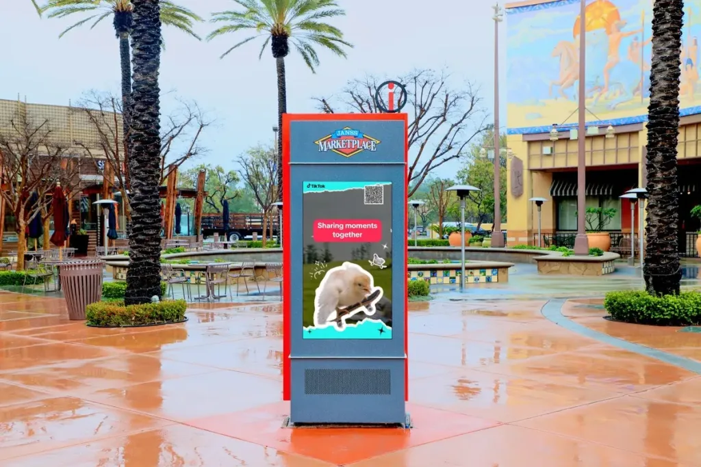 grey outdoor digital interactive kiosk at Janns Marketplace in California during the day, showing a digital ad from TikTok with a large bird.