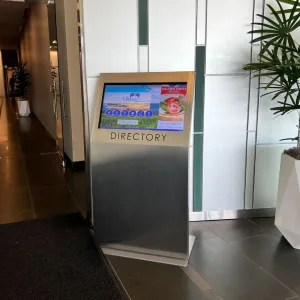 touchsource-stainless-steel-alta-kiosk-32-inch-touchscreen - TouchSource - TouchSource Touchscreen directory kiosk in a modern lobby, with a 'DIRECTORY' label on the metal pedestal and a colorful display on the screen.